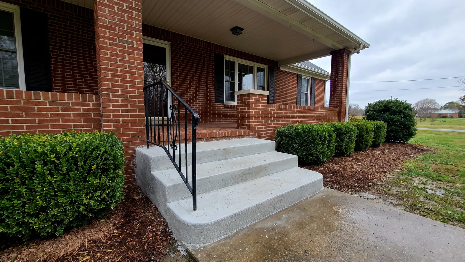 Newly poured concrete front steps with rounded nosings leading up to the porch of a brick home in the Upstate of South Carolina